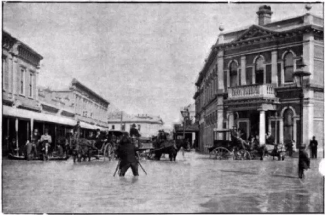 Market Street North in Blenheim submerged under floodwaters, showing buildings lining the roadway.